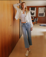 Woman in a white shirt and blue jeans standing in a room with wooden walls and a desk.